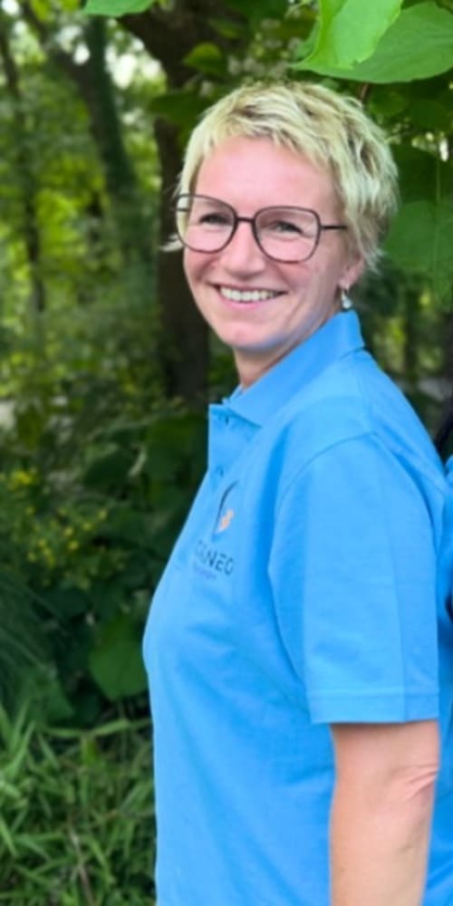 Ein Portaitbild von Frau Haas Ein Portaitbild von Frau Haas in Curaneo T-Shirt. Sie ist blond, hat kurze Haare und trägt eine Brille.
