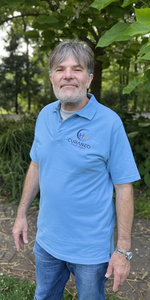 Portaitbild von Herrn Baier Ein Portaitbild von Herrn Baier in Curaneo T-Shirt. Er hat graues Haar und Bart.