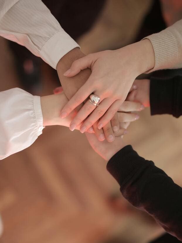 Fünf unterschiedliche Hände liegen aufeinander, um den Teamspirit zu unterstreichen.