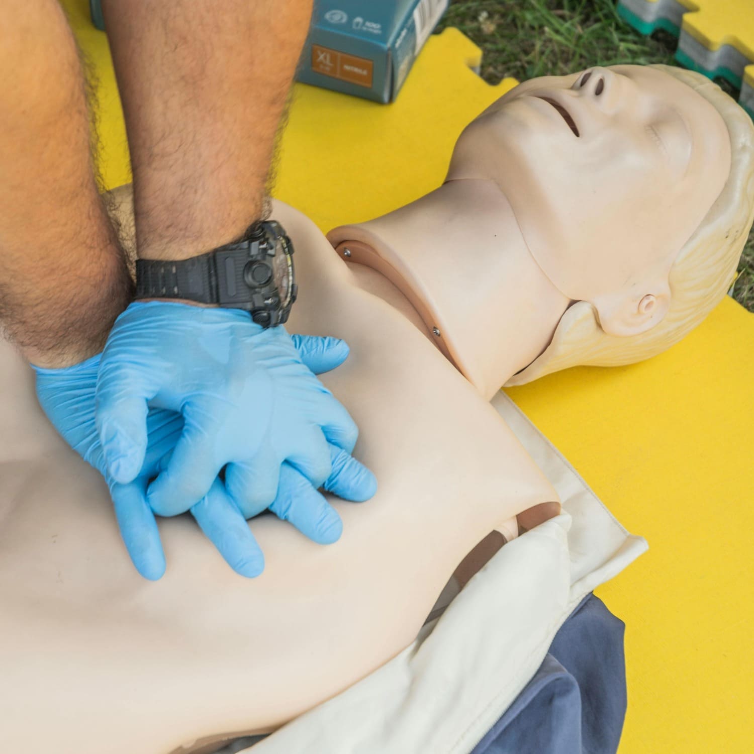 Erste-Hilfe-Kurse bei Curaneo Pflege Ein Ersthelfer mit Handschuhen übt eine Herzdruckmassage an einer Übungspuppe für Erste-Hilfe.